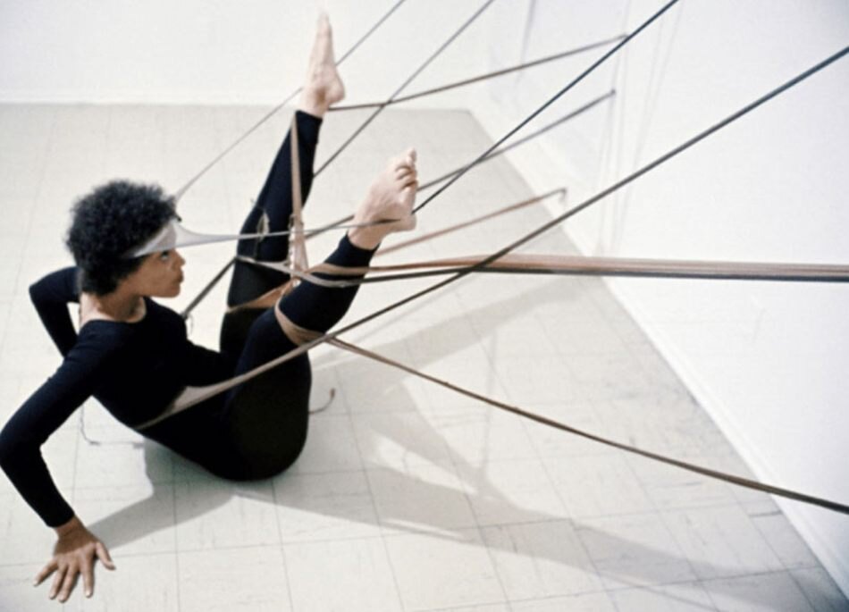Maren Hassinger, in black, stretches on the floor among taut lines of Senga Nengudi's R.S.V.P. sculpture anchored to the wall.